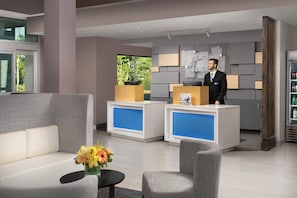 A hotel reception area with a reception desk, seating area, and a refrigerator stocked with beverages. - Holiday Inn Express and Suites North Brunswick by IHG (North Brunswick)