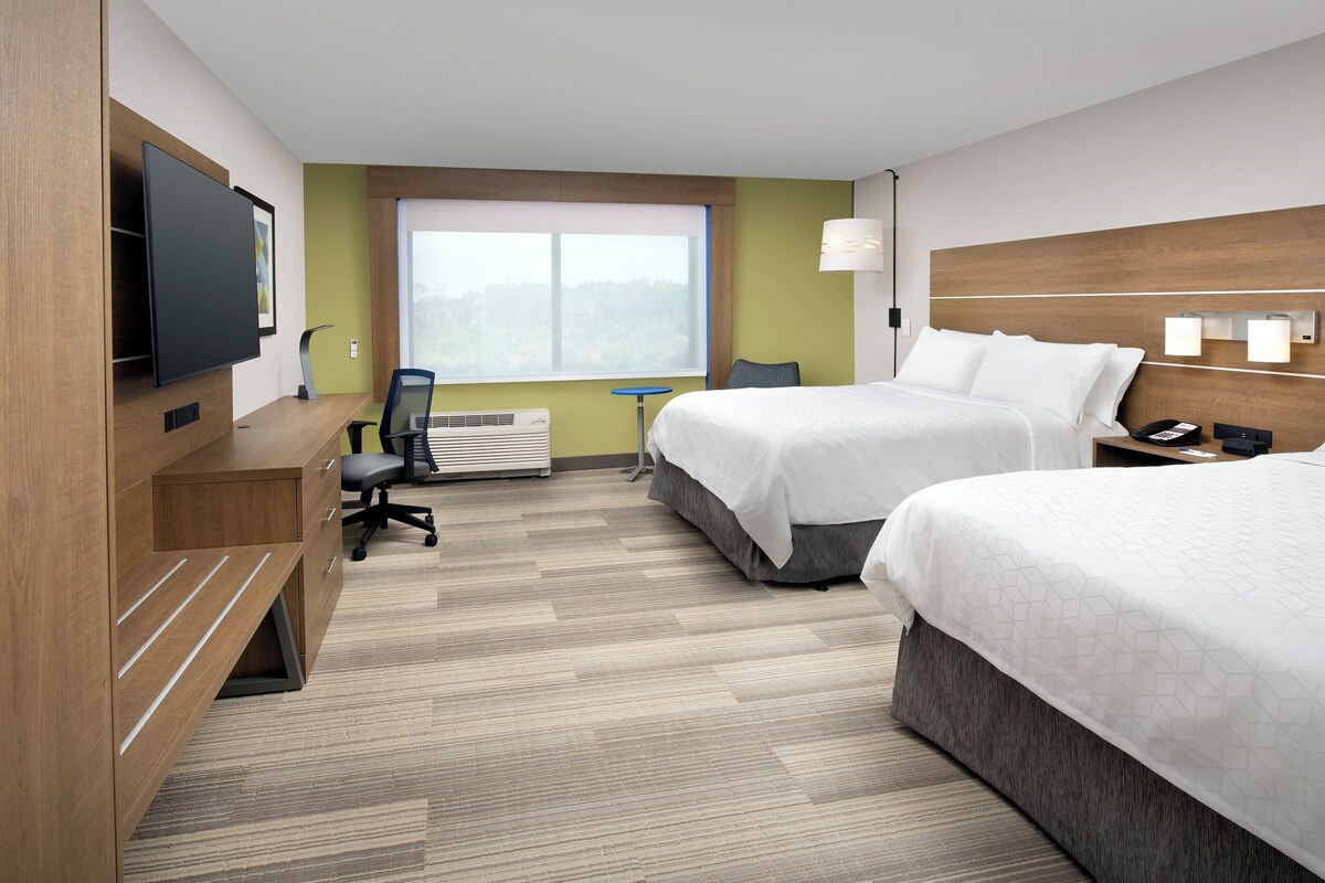 A hotel room with two beds, a desk, a chair, a TV, and a window with a view.