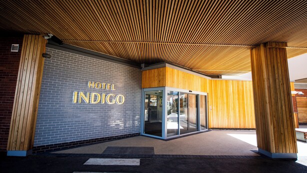 Het exterieur van Hotel Indigo, met een modern ontwerp, met een gevel van baksteen, een houten lambrisering en glazen entreedeuren.