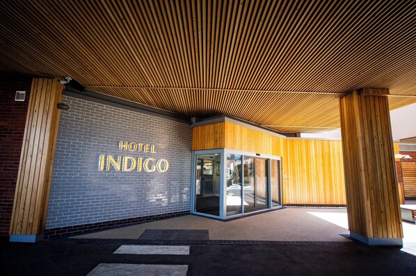 Exterior del Hotel Indigo con diseño moderno, que presenta fachada de ladrillo, techo de listones de madera y puertas de entrada de vidrio.