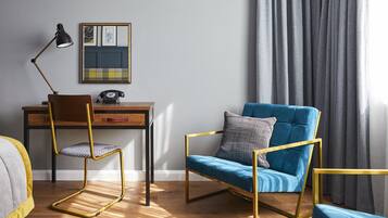 A room with a wooden desk, a blue armchair, a yellow chair, a black lamp, and a telephone.