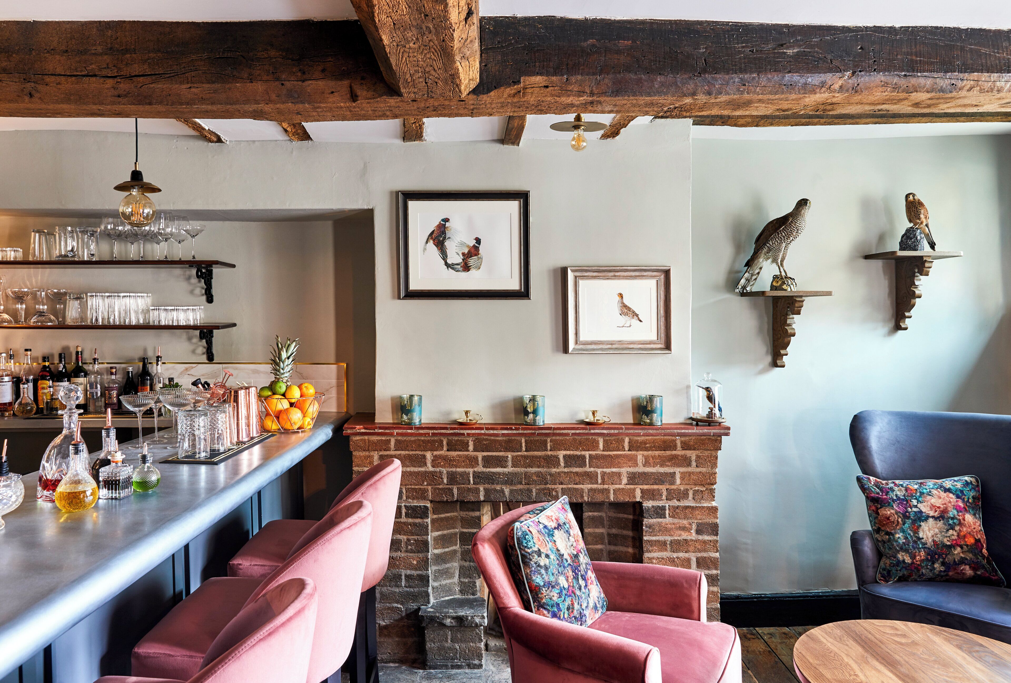 A bar area with shelves of glasses and bottles, a brick fireplace, and a seating area with chairs and a sofa.
