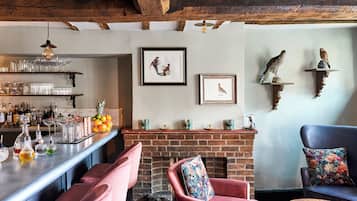 A bar area with shelves of glasses and bottles, a brick fireplace, and a seating area with chairs and a sofa.