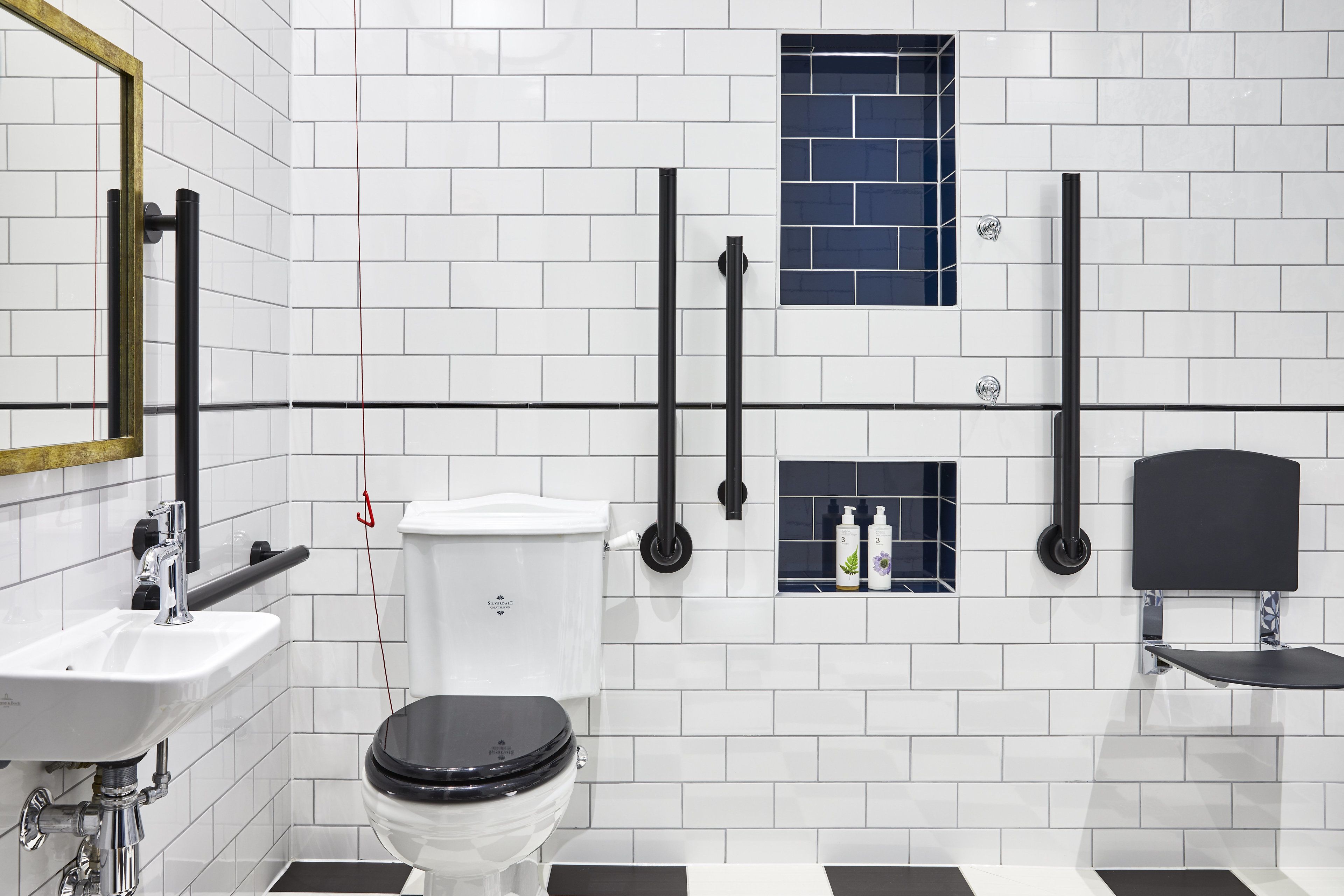 A modern bathroom with white tiled walls, a black toilet, a sink, and a mirror.