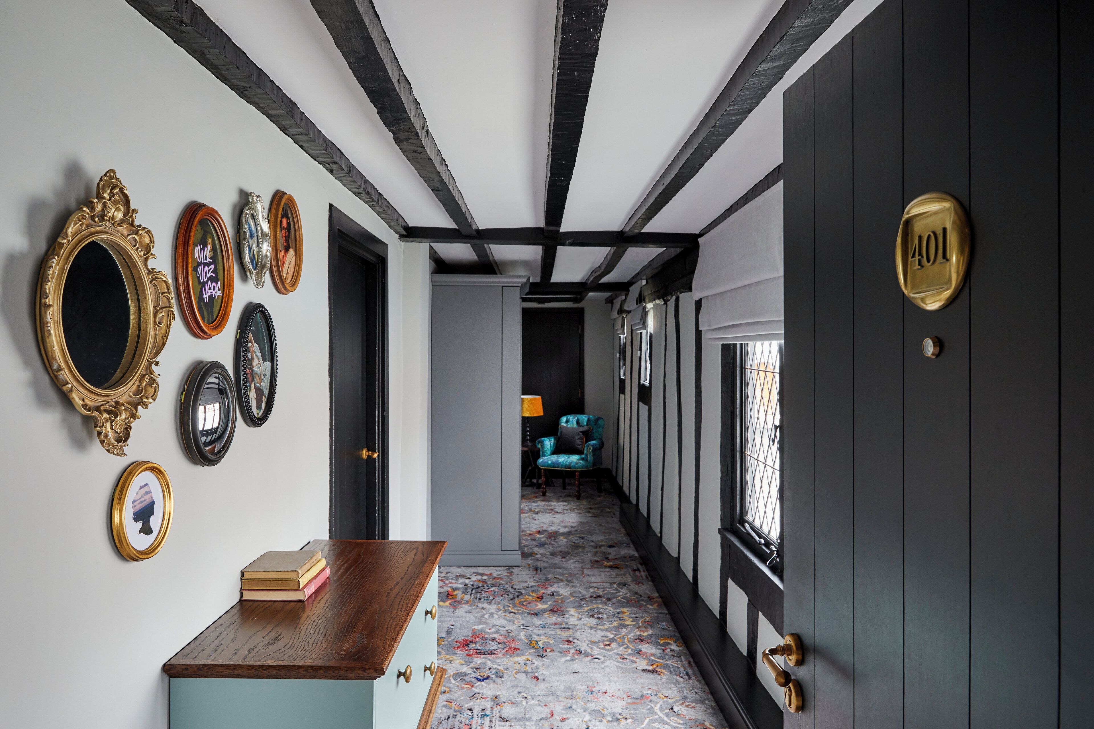 A hallway with a wooden desk, a blue chair, and a door with a number plate.
