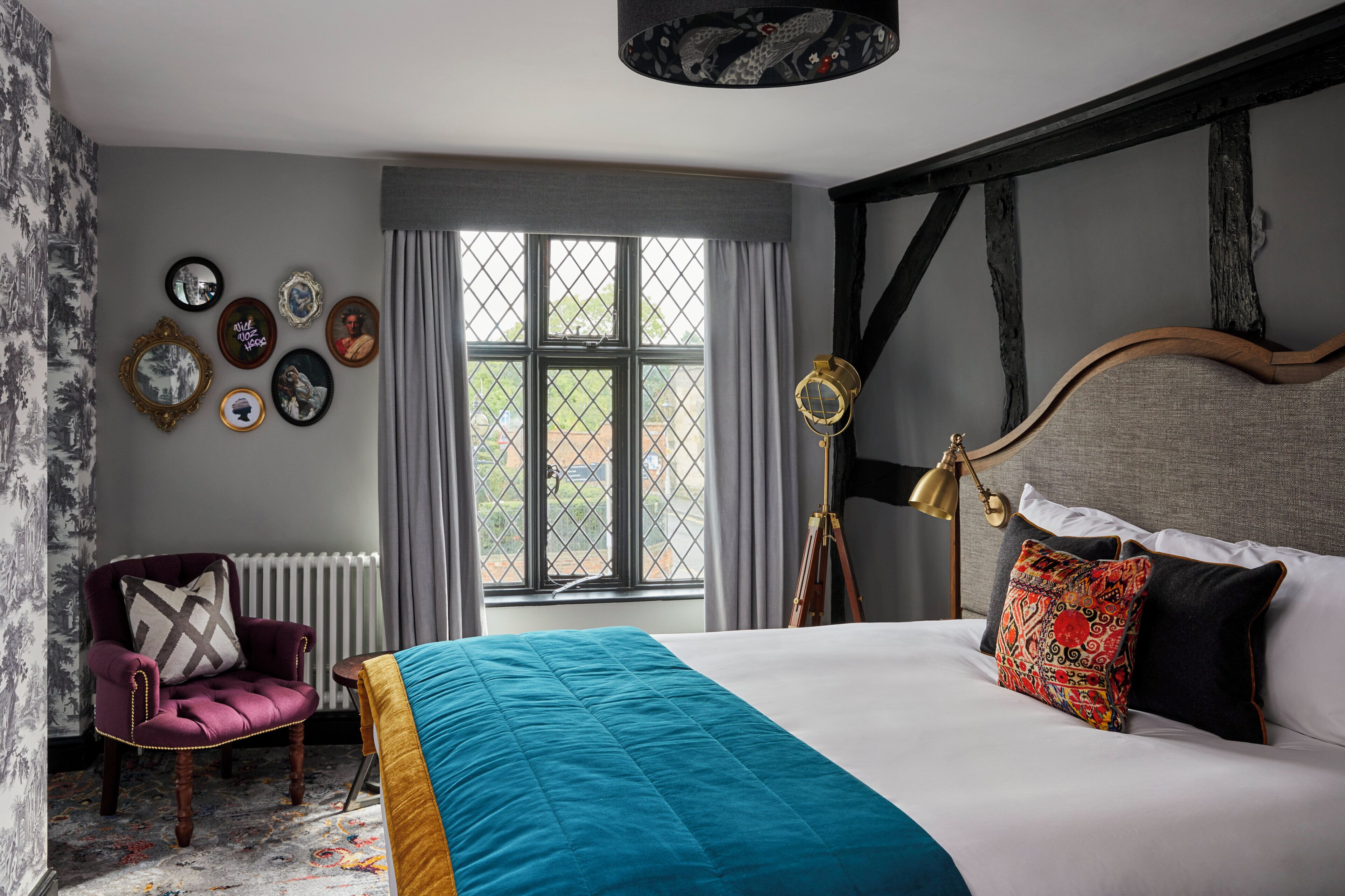 A bedroom with a large bed, a chair, a window, and various wall decorations.