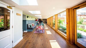 Un couloir avec un plancher en bois, un canapé bleu orné de coussins à motifs floraux et un fauteuil rouge.