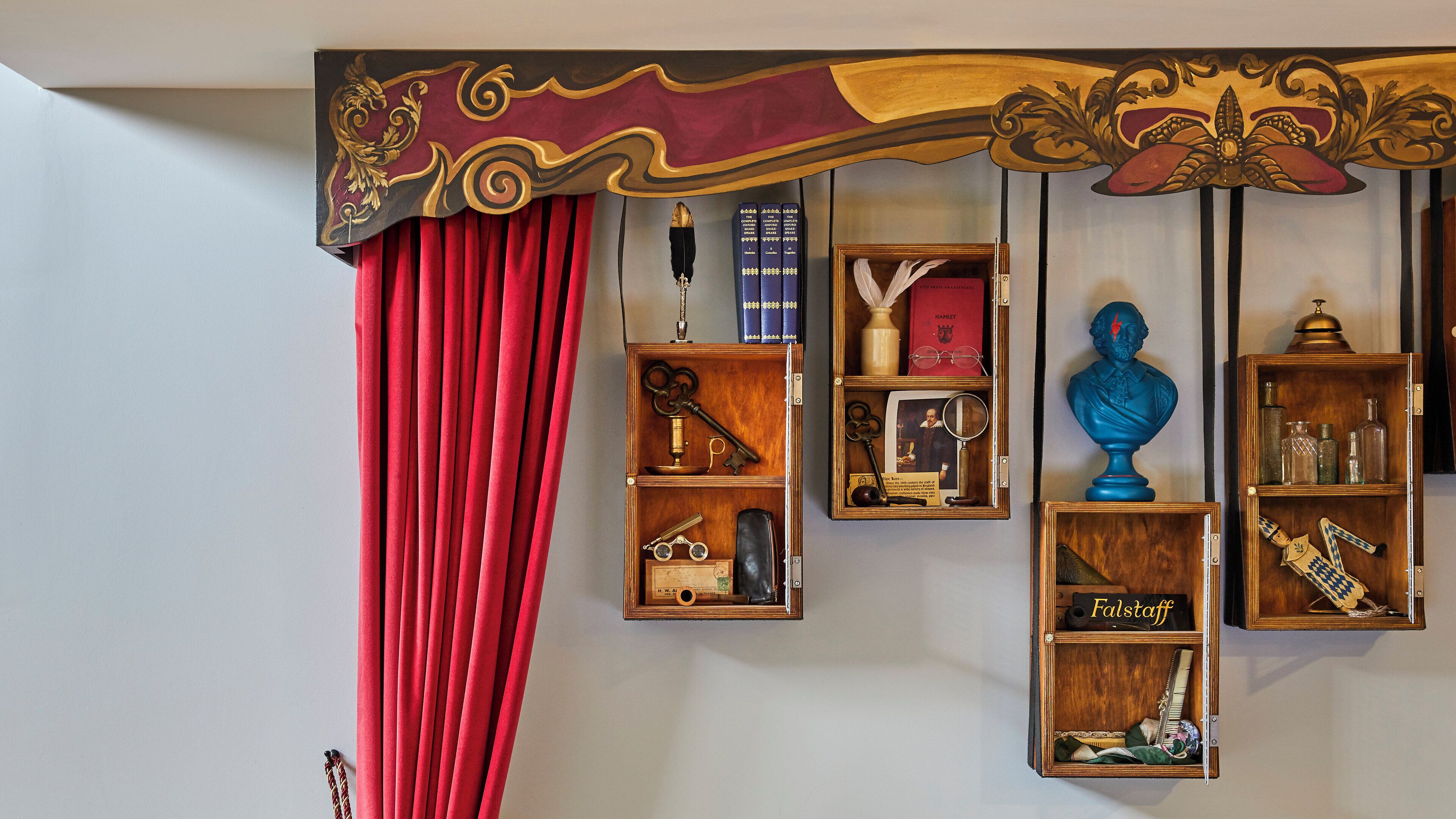 Una habitación con cortina roja, estanterías de madera con diversos objetos y un techo decorativo.
