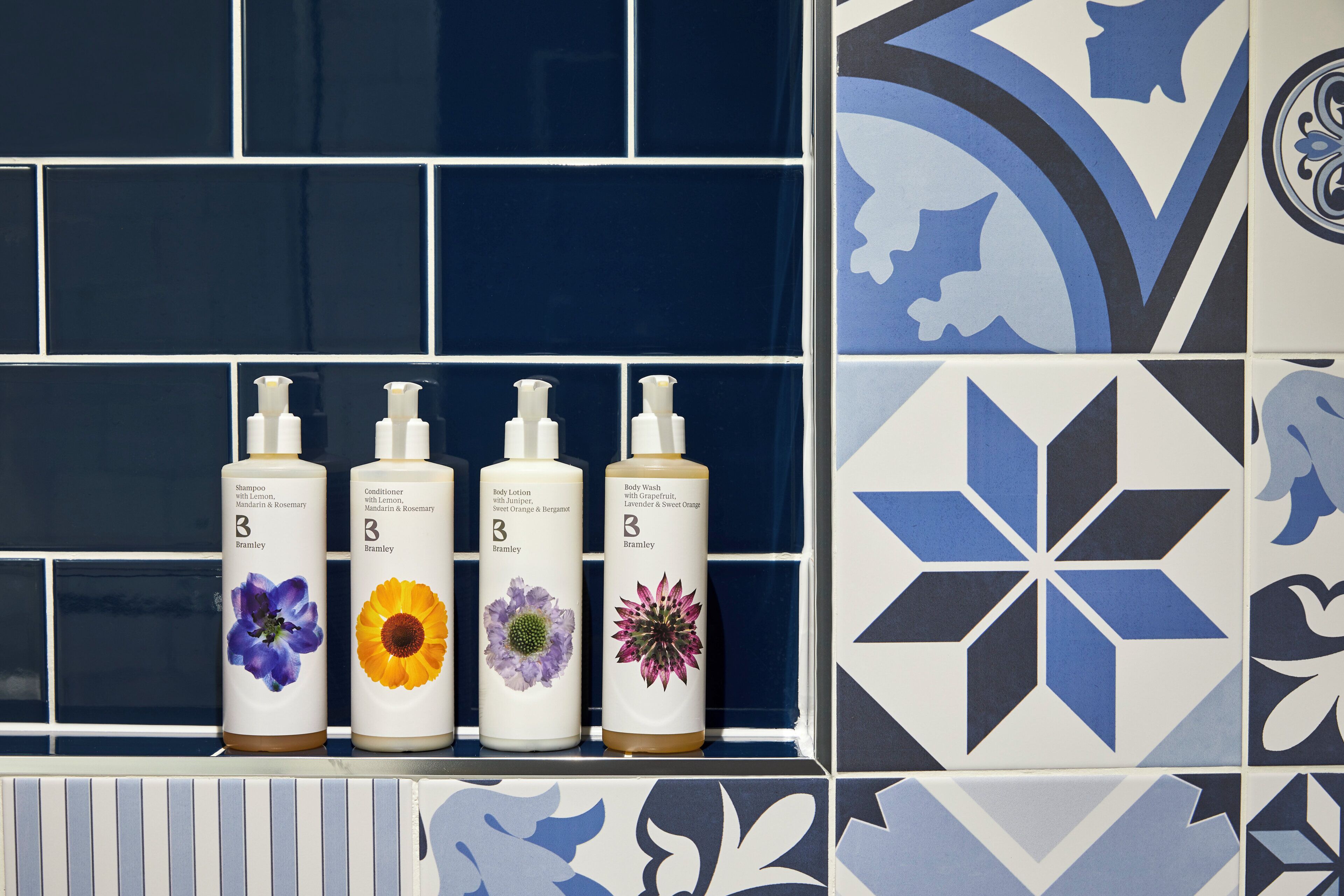 Quatro frascos de produtos de higiene pessoal sobre um prateleira azulejada.