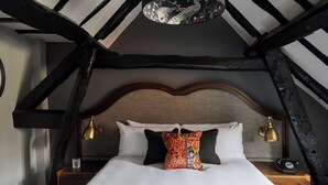 Een bed met een houten hoofdbord, twee bedlampen, een kussen met een patroon en een telefoon op een nachtkastje van hout.