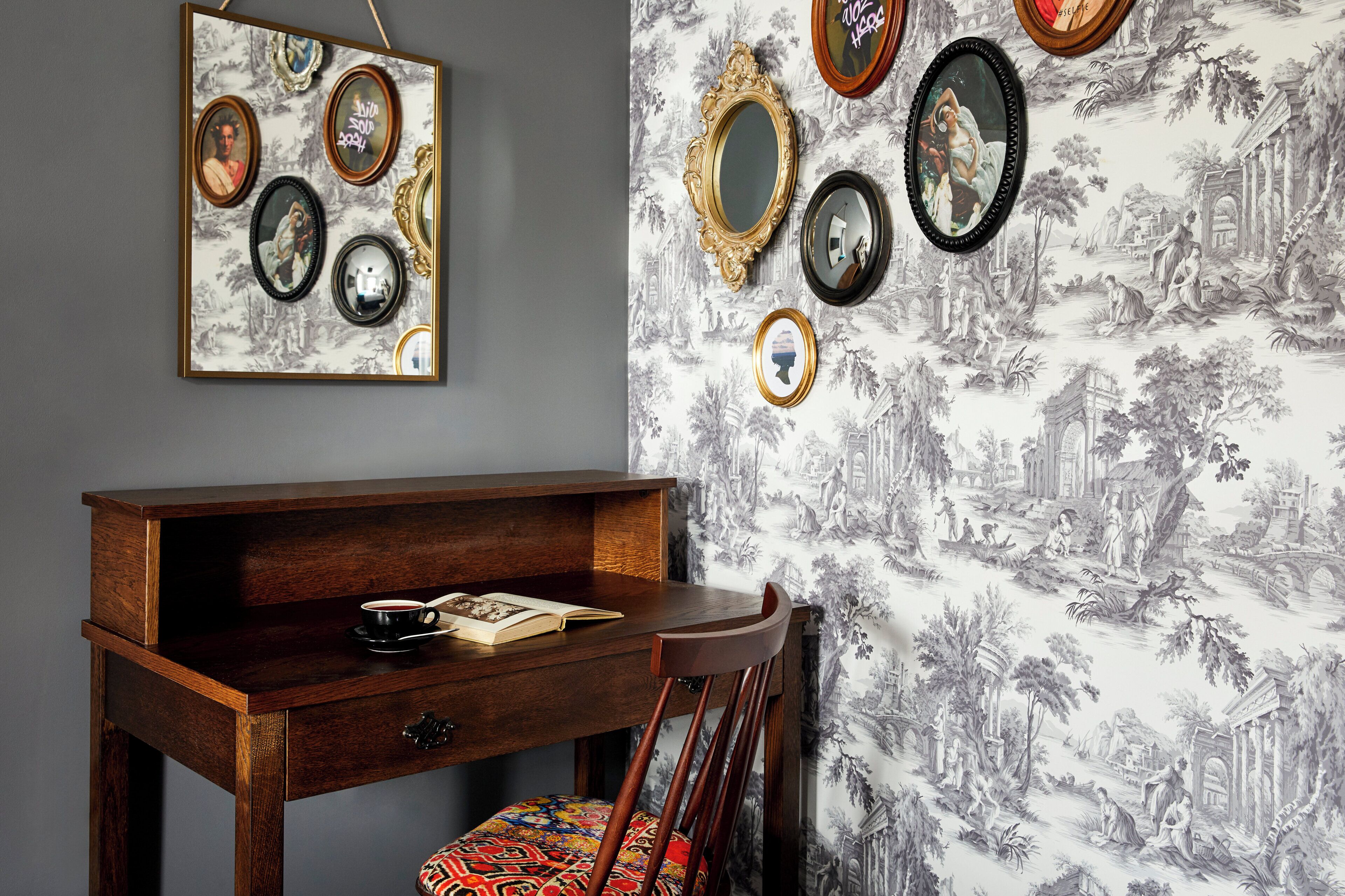 Une pièce comprenant un bureau, une chaise et un mur décoré de miroirs encadrés et d’un papier peint à motifs.