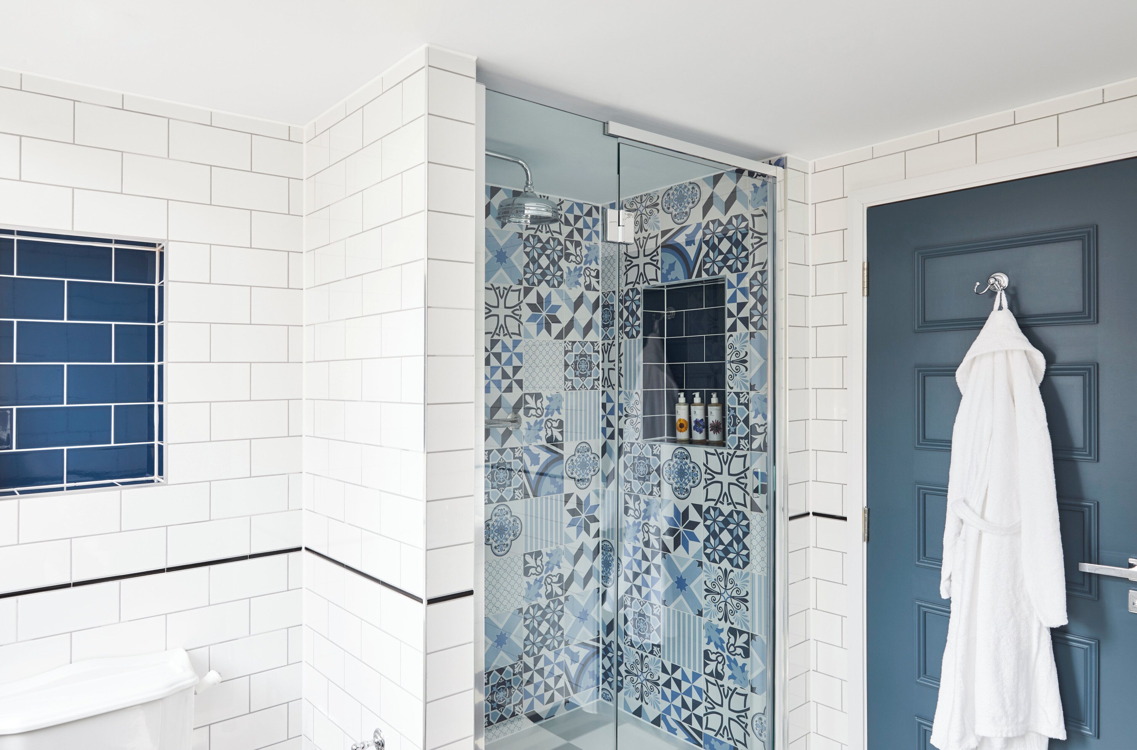 A bathroom with white tiles, a blue door, and a shower with patterned tiles.
