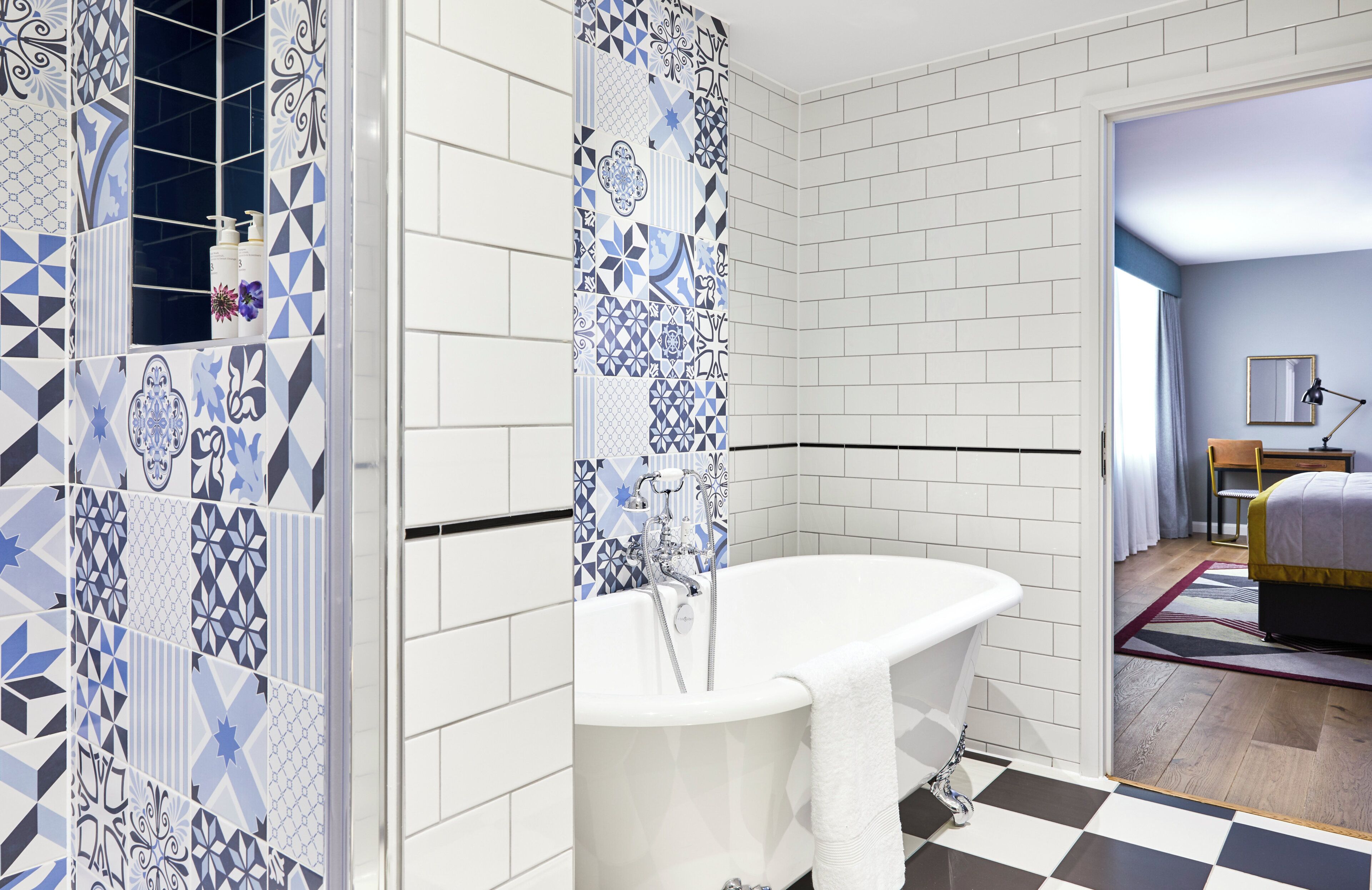 Un bagno con una vasca da bagno bianca, una doccia con tenda da bagno a motivi blu e bianchi e un pavimento a scacchi.