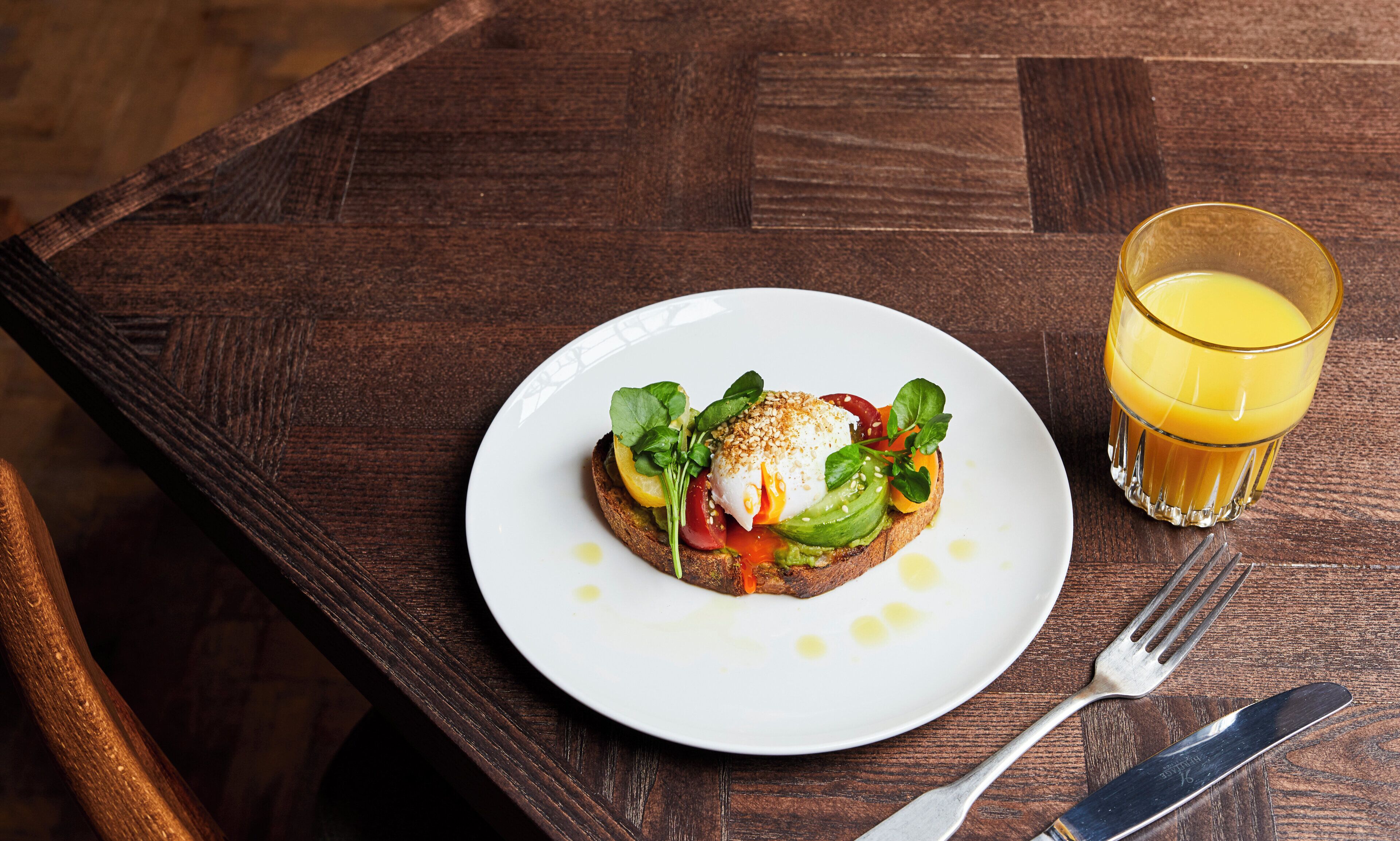 A breakfast plate with toast, egg, and vegetables, and a glass of orange juice on a wooden table.