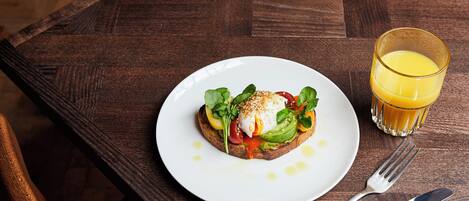 A breakfast plate with toast, egg, and vegetables, and a glass of orange juice on a wooden table.
