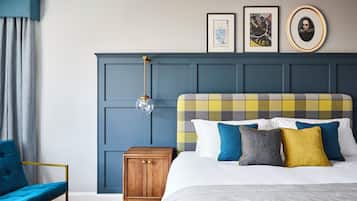 Un dormitorio con cabecera azul, cama con ropa de cama escocesa, mesita de noche de madera y sillón azul.