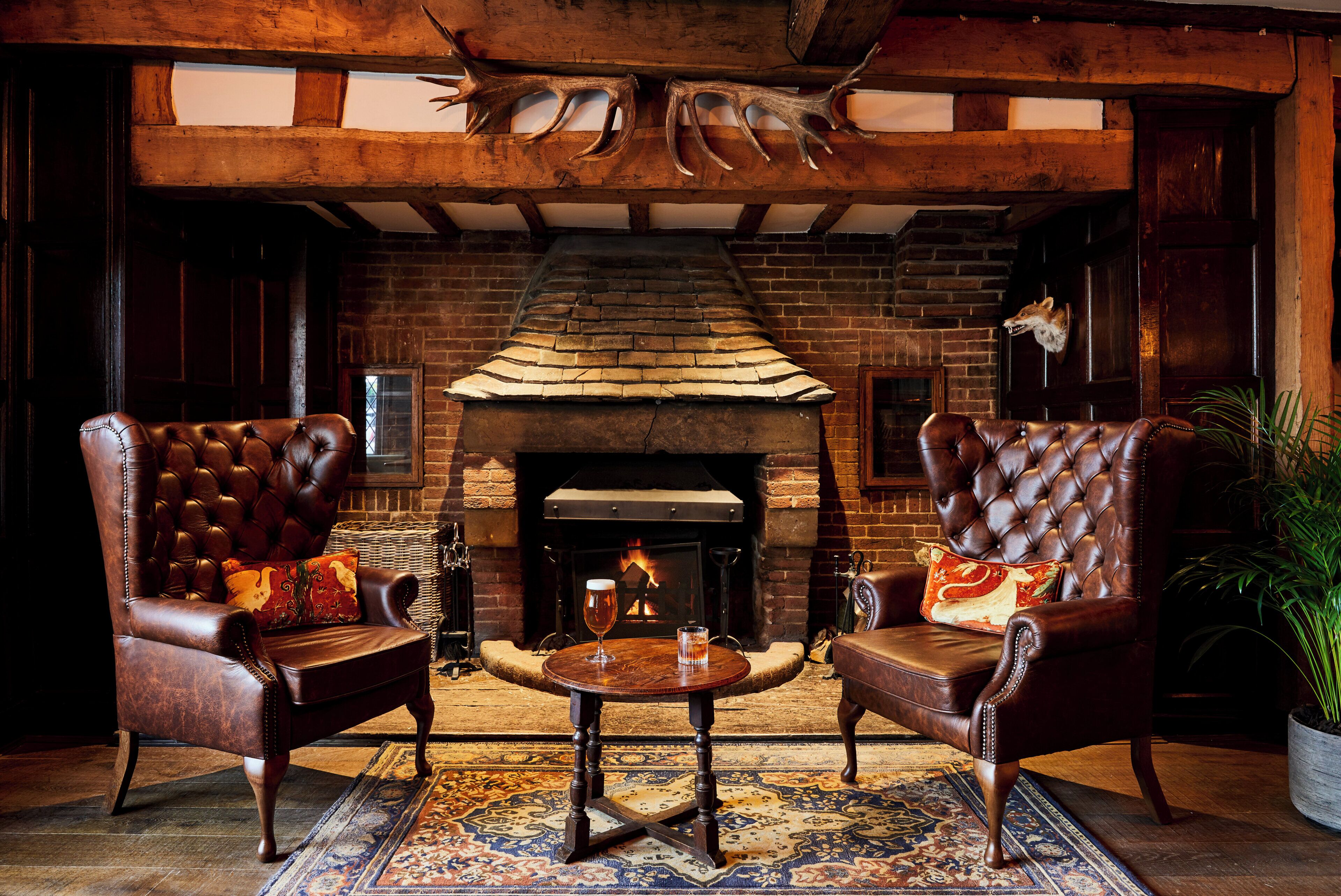 A cozy lounge area with leather armchairs, a small round table, and a brick fireplace.