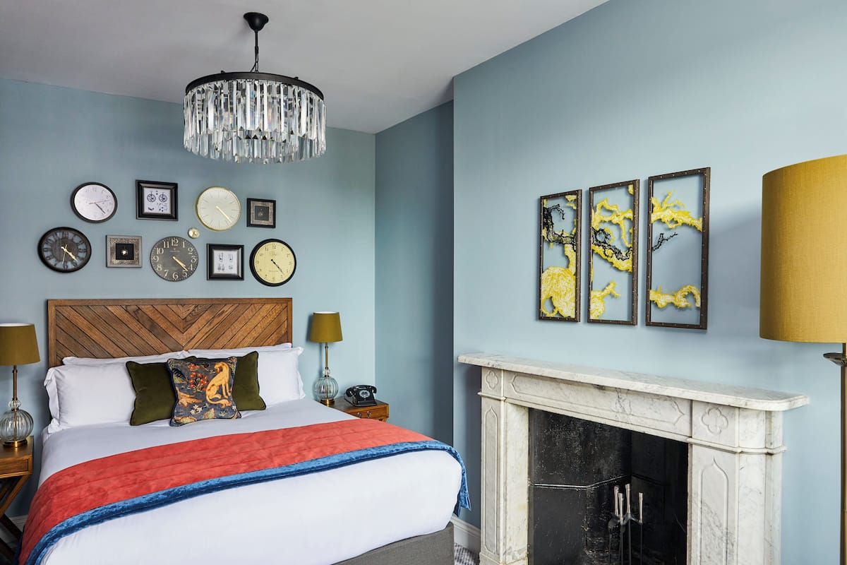 A bedroom with a bed, a chandelier, a fireplace, and wall art.
