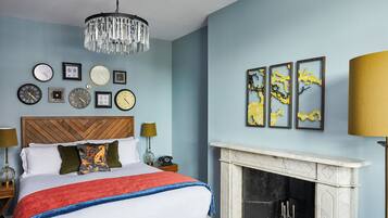 A bedroom with a bed, a chandelier, a fireplace, and wall art.