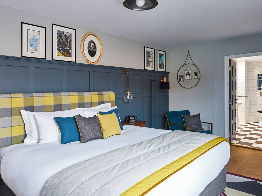 A hotel room with a large bed, a bedside table, a chair, and a view of the bathroom.