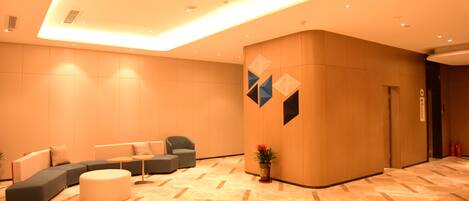 A modern lobby with a sectional sofa, a round ottoman, and a potted plant.