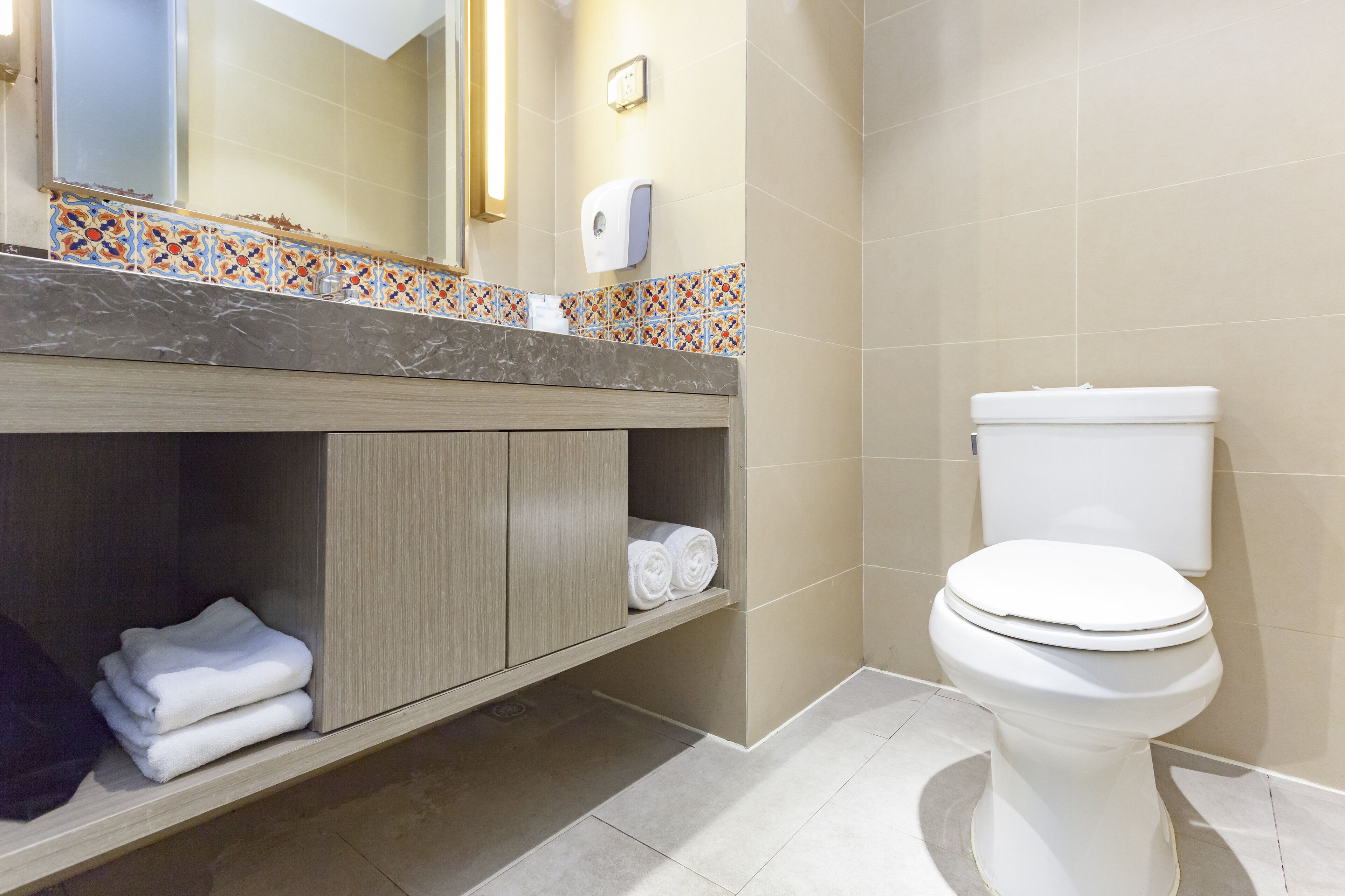 Un baño con inodoro, lavamanos y encimera de mármol, y un espejo.
