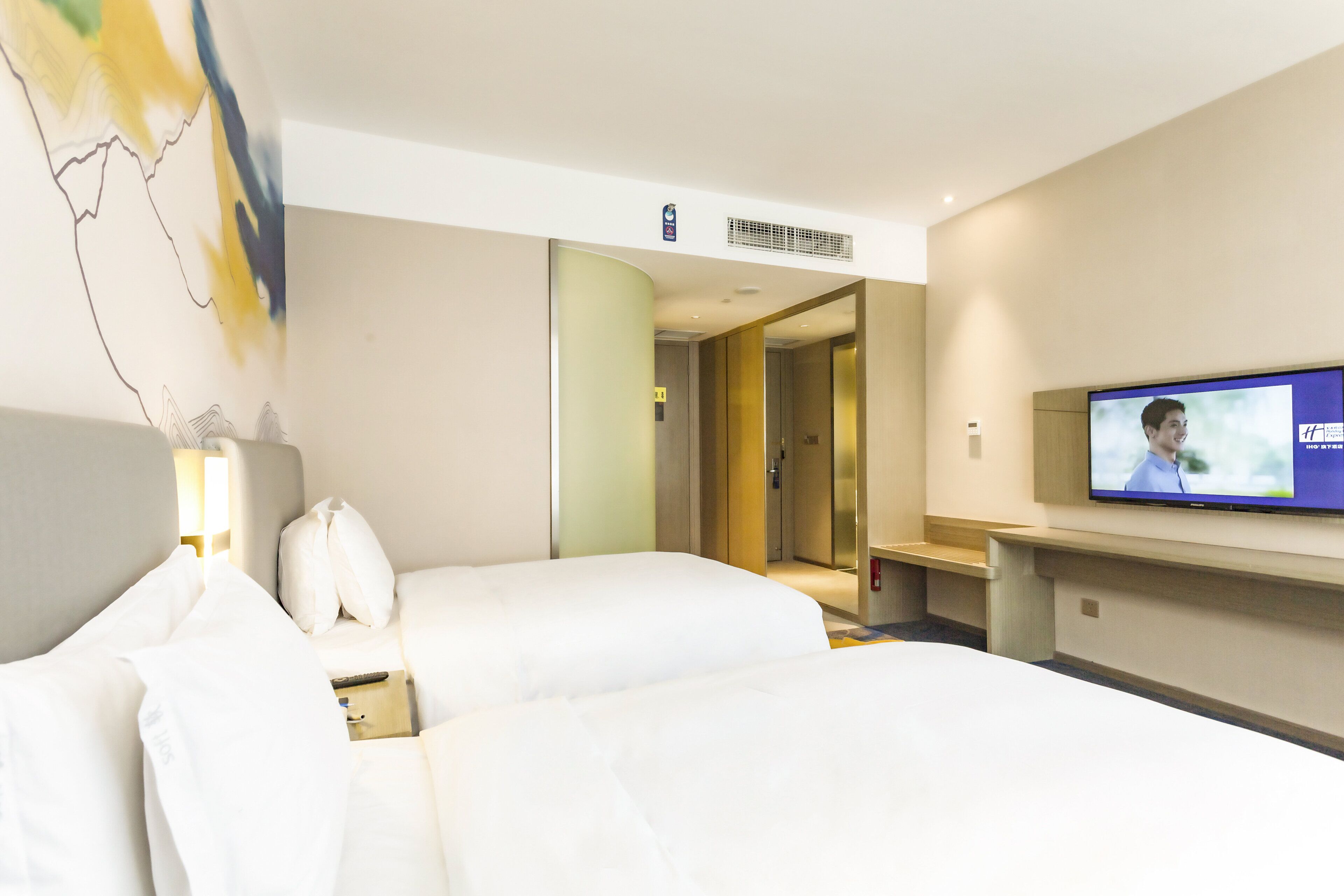 A hotel room with two beds, a television, a desk, and a bathroom visible through an open door.