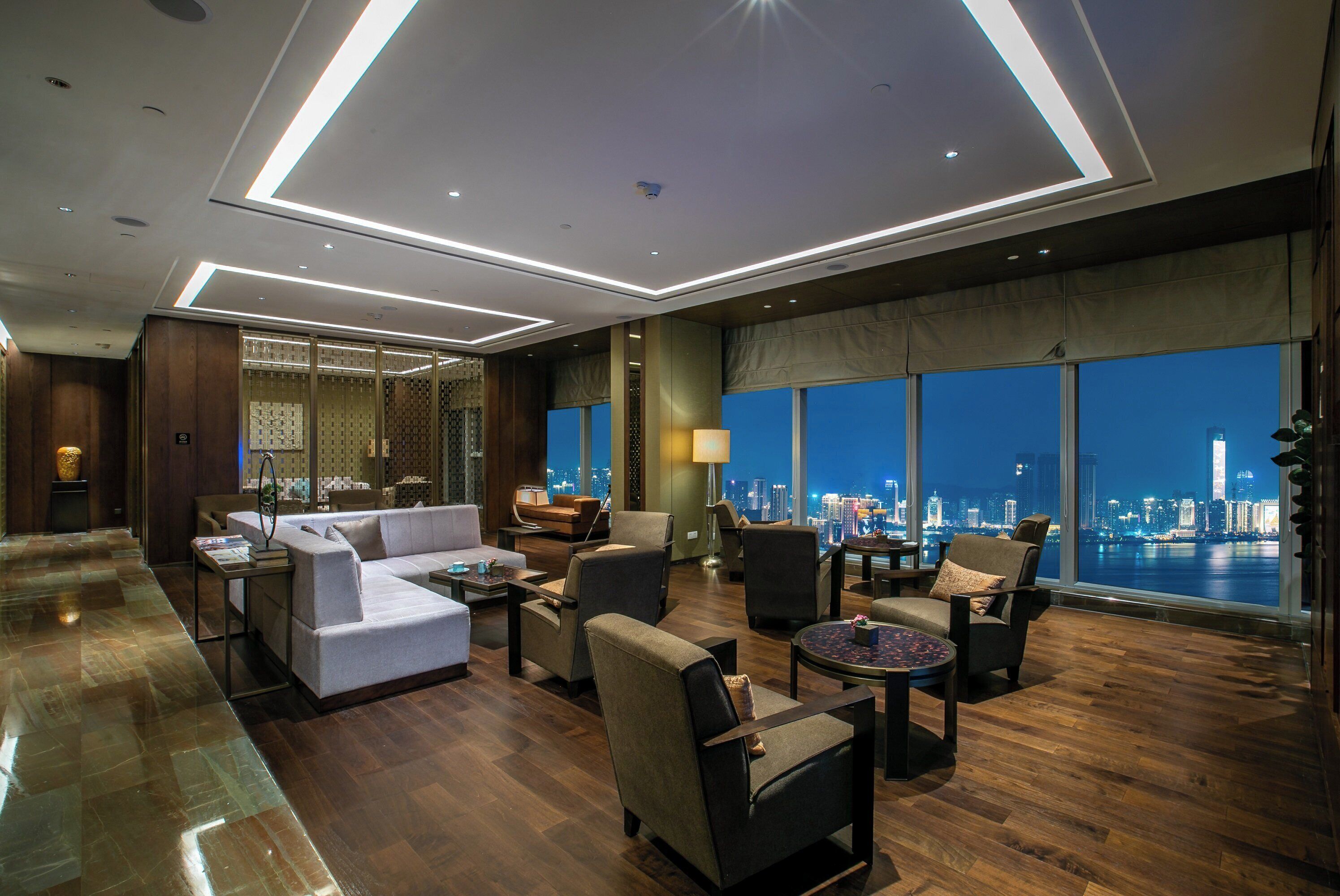 A modern hotel lobby with a city view, a seating area with sofas and armchairs, and a large window overlooking the skyline.