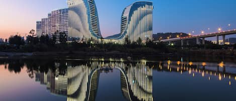 Un bâtiment moderne à la façade incurvée, qui se reflète dans l’eau, avec un pont en arrière-plan.