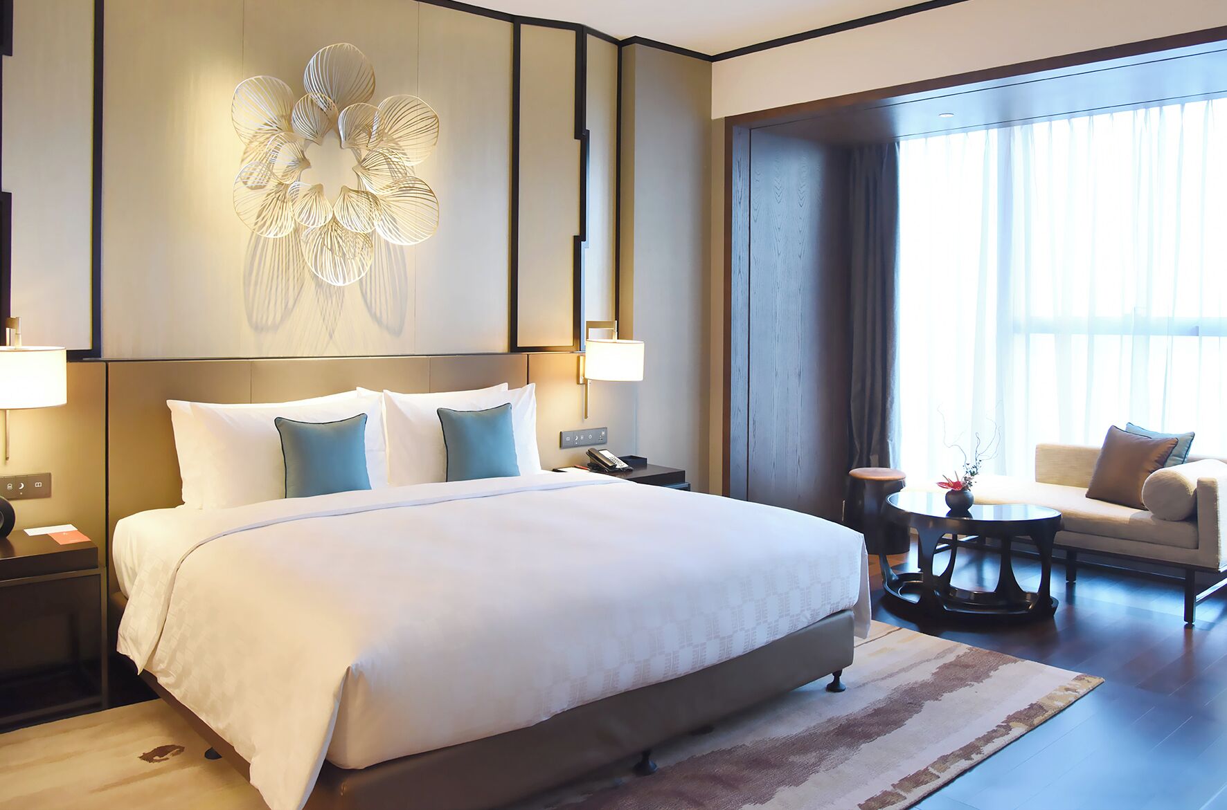 A hotel room with a large bed, a sofa, a small table, and a decorative wall piece.
