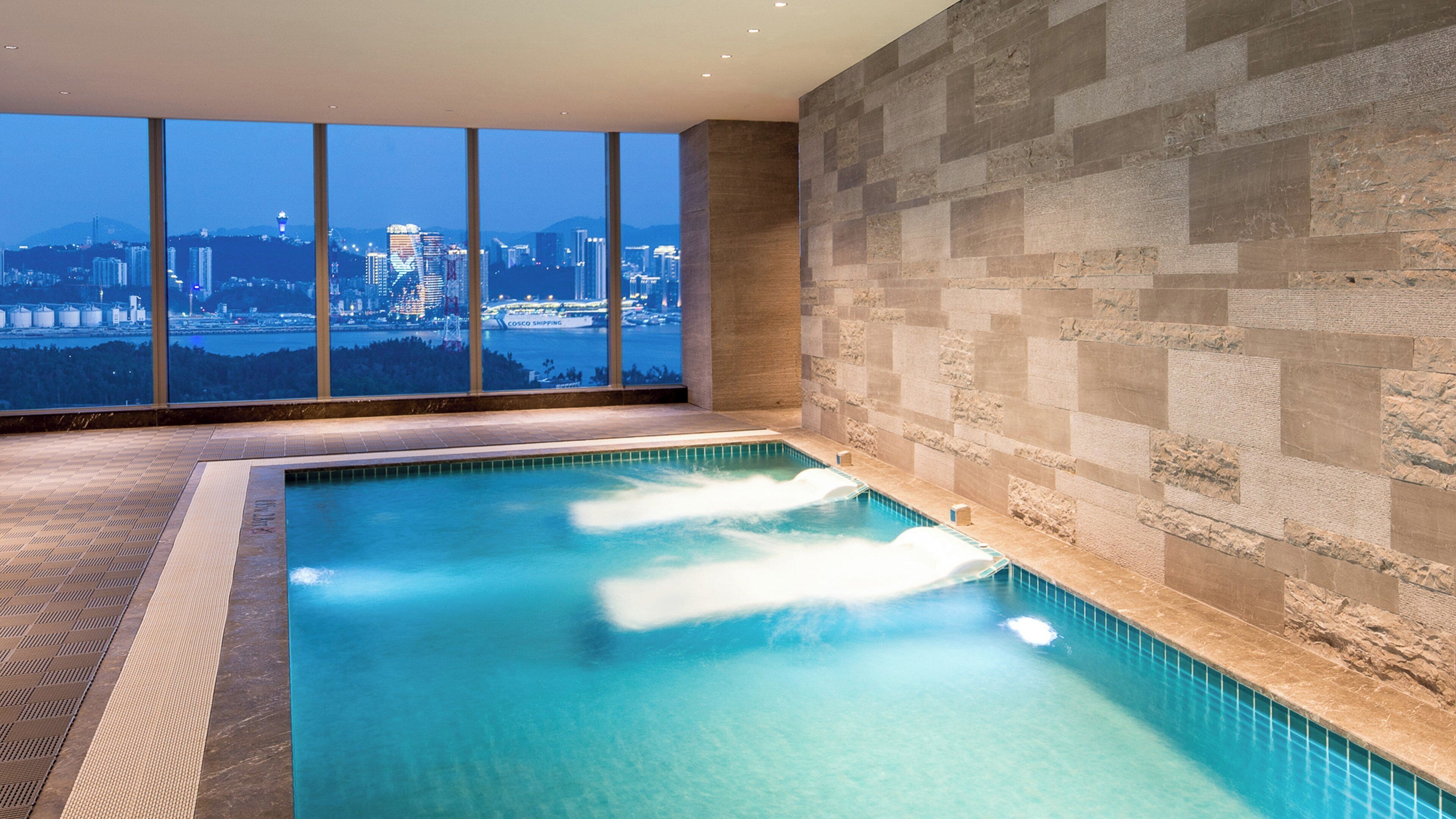 A swimming pool with a cityscape view, stone wall, and tiled floor.