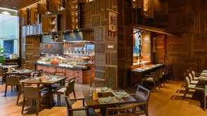 A restaurant with wooden decor, a central counter with dishes, and multiple dining tables and chairs. - HUALUXE Xiamen Haicang Harbour View by IHG (Xiamen)