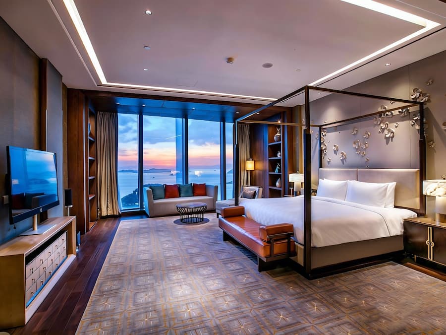Una habitación de hotel moderna con una cama grande, televisión, sofá y vistas al atardecer.