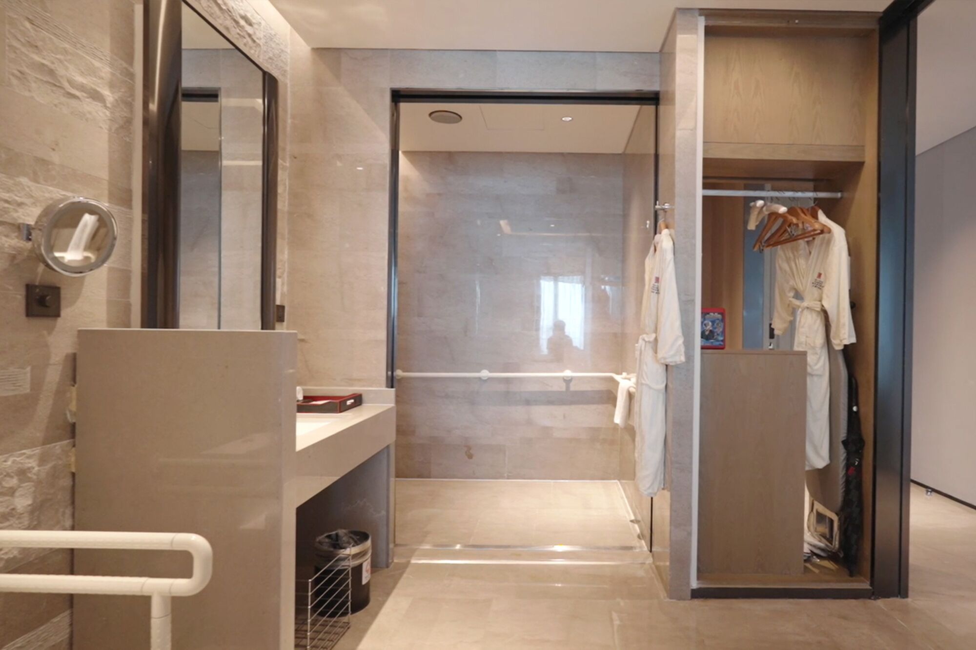 A modern bathroom with a glass shower enclosure, a towel rack, and a visible trash bin.