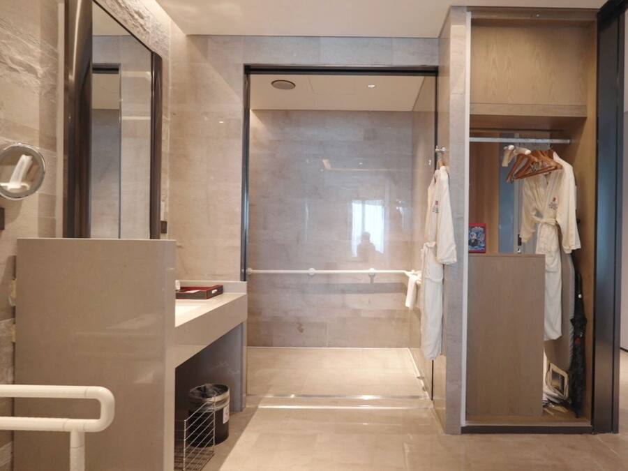 A modern bathroom with a glass shower enclosure, a towel rack, and a visible trash bin.