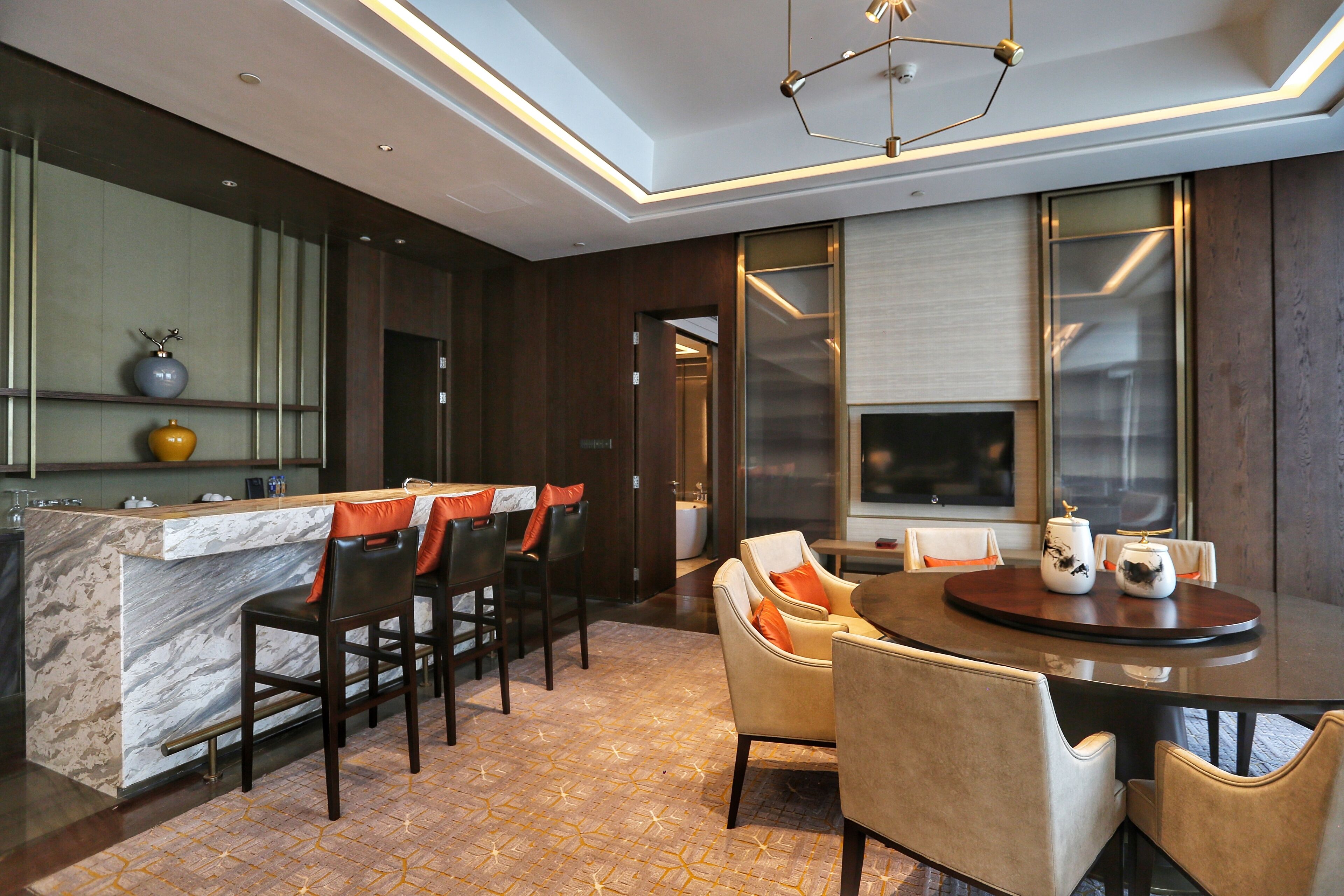 A modern dining area with a marble bar, dark wooden chairs, and a round table with orange cushions.