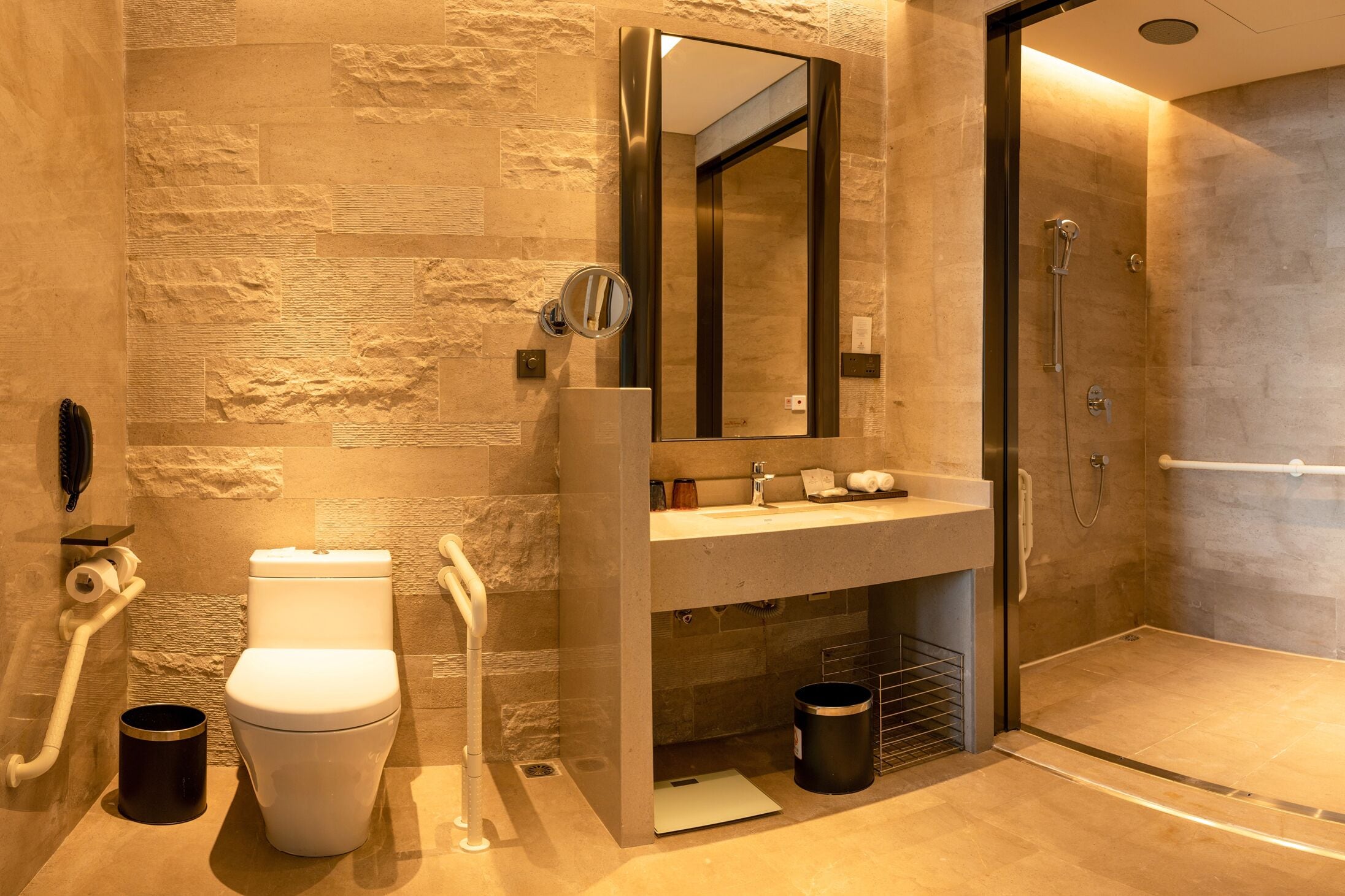 A modern bathroom with a stone-textured wall, a white toilet, a sink with a mirror, and a walk-in shower.
