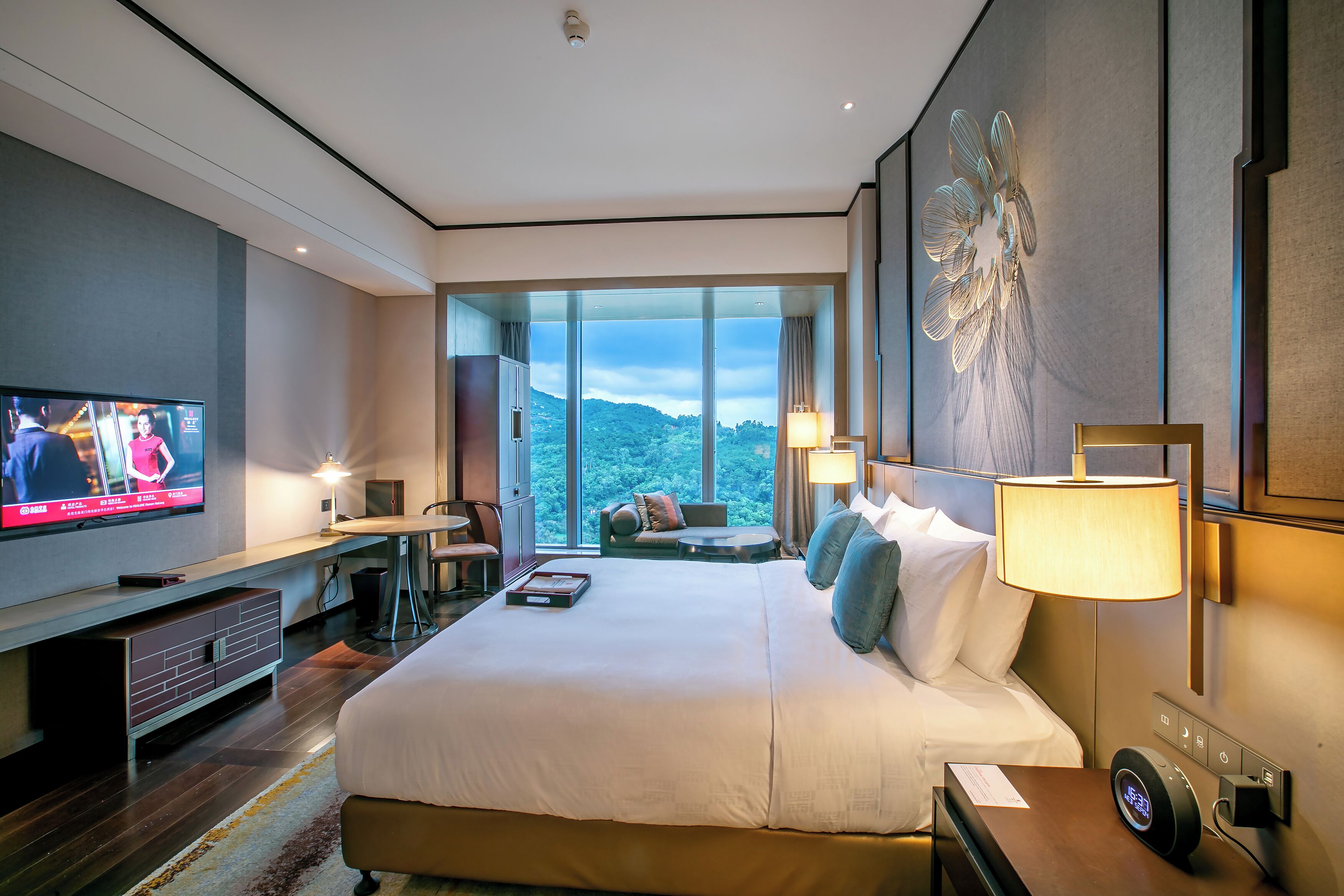 A modern hotel room with a large bed, a desk, a television, and a view of the outdoors.