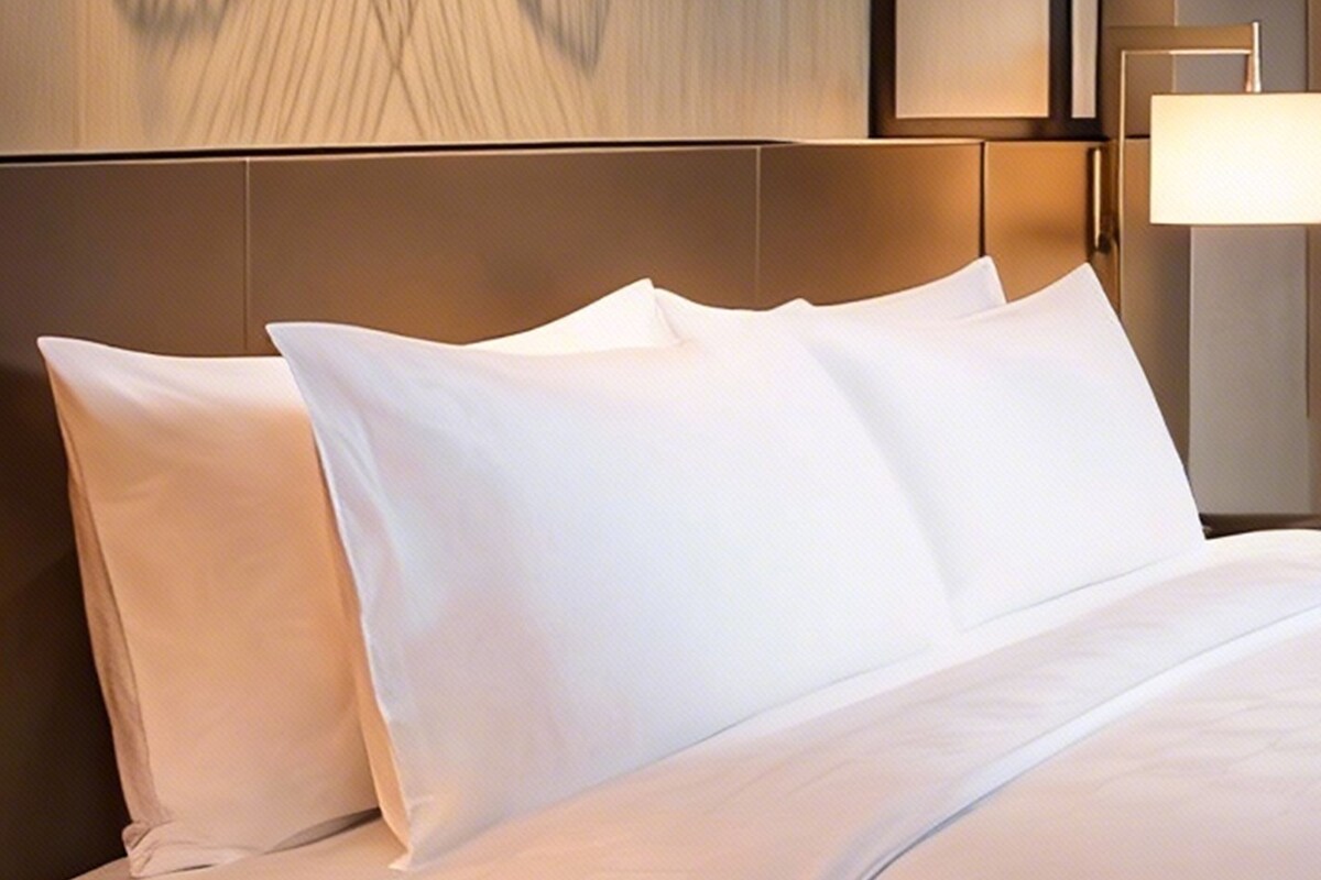 A hotel room with a neatly made bed, a headboard, and a wall-mounted lamp.