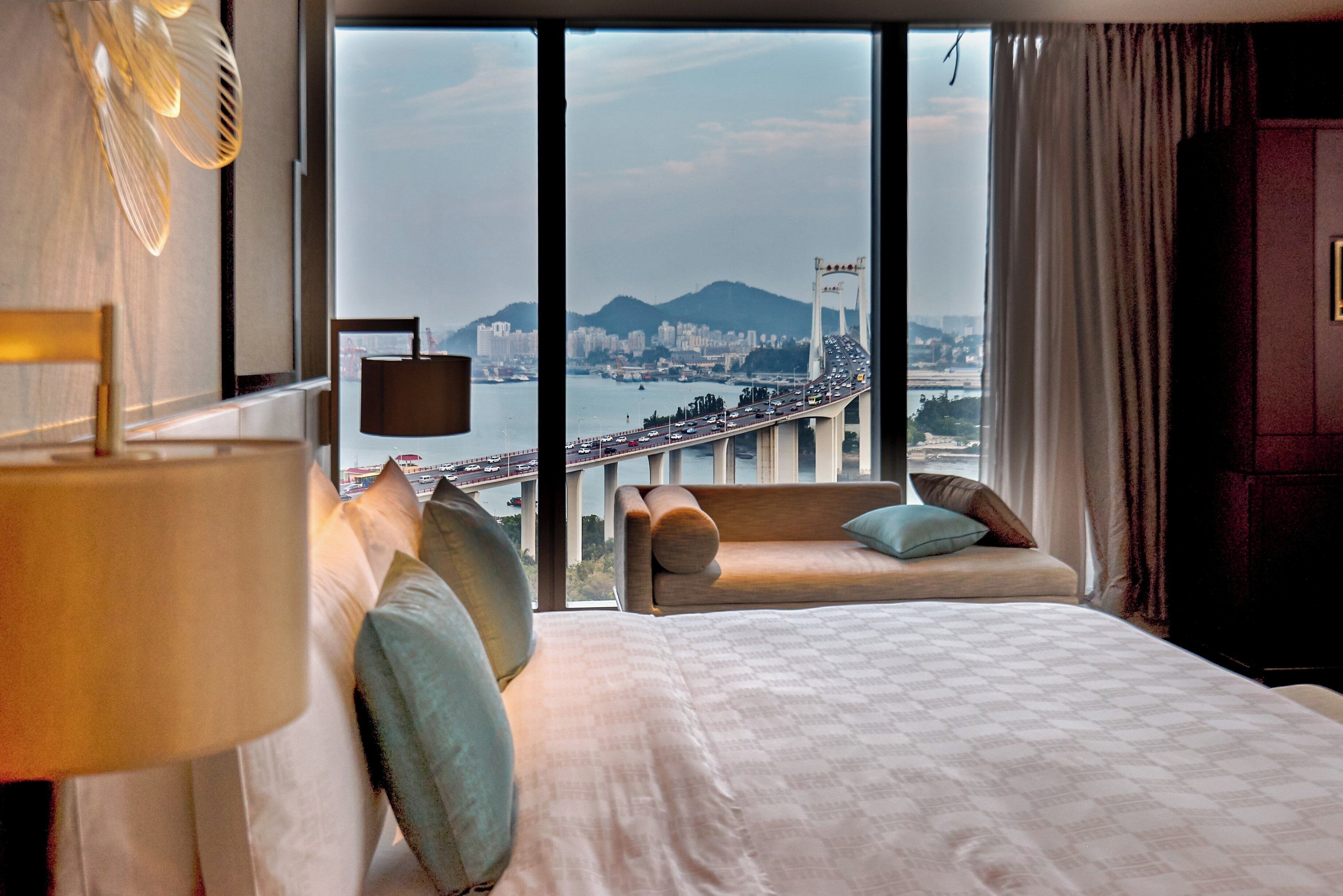 Une chambre d’hôtel avec une grande fenêtre, un lit, un canapé et une lampe.