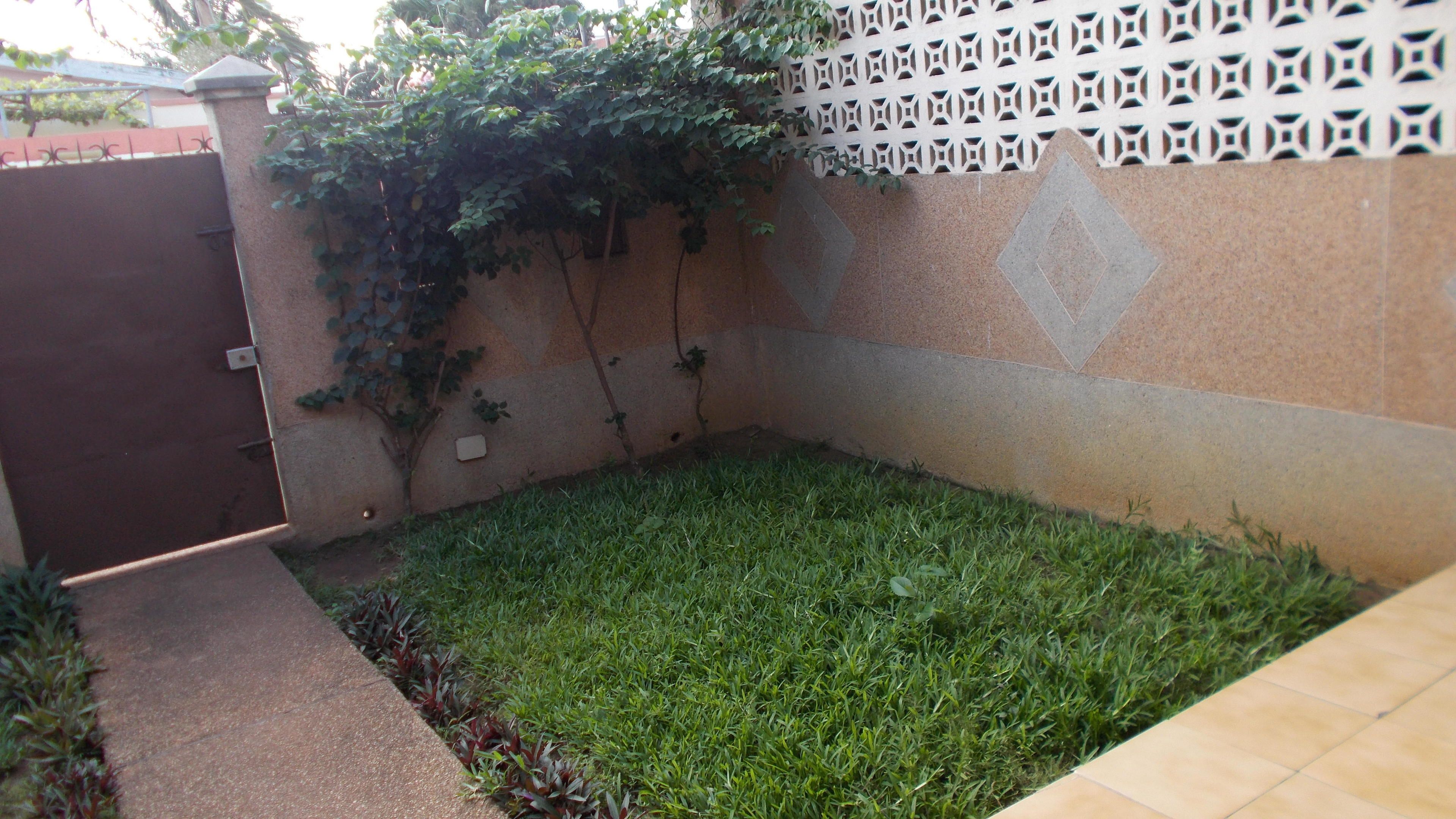 A small, enclosed garden area with a paved path, a metal gate, and a decorative wall with geometric patterns.