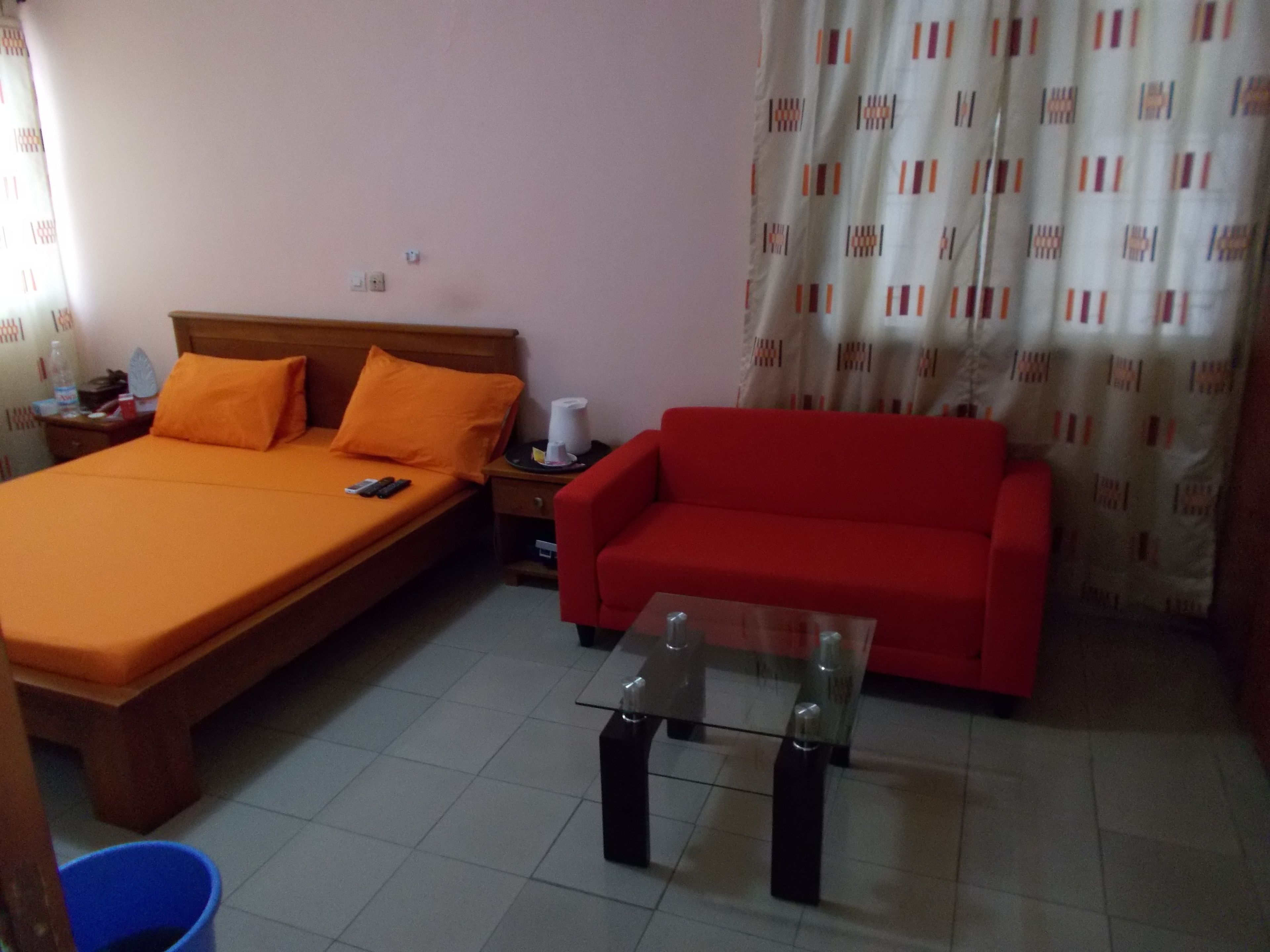 A room with a bed, a red sofa, and a glass table.