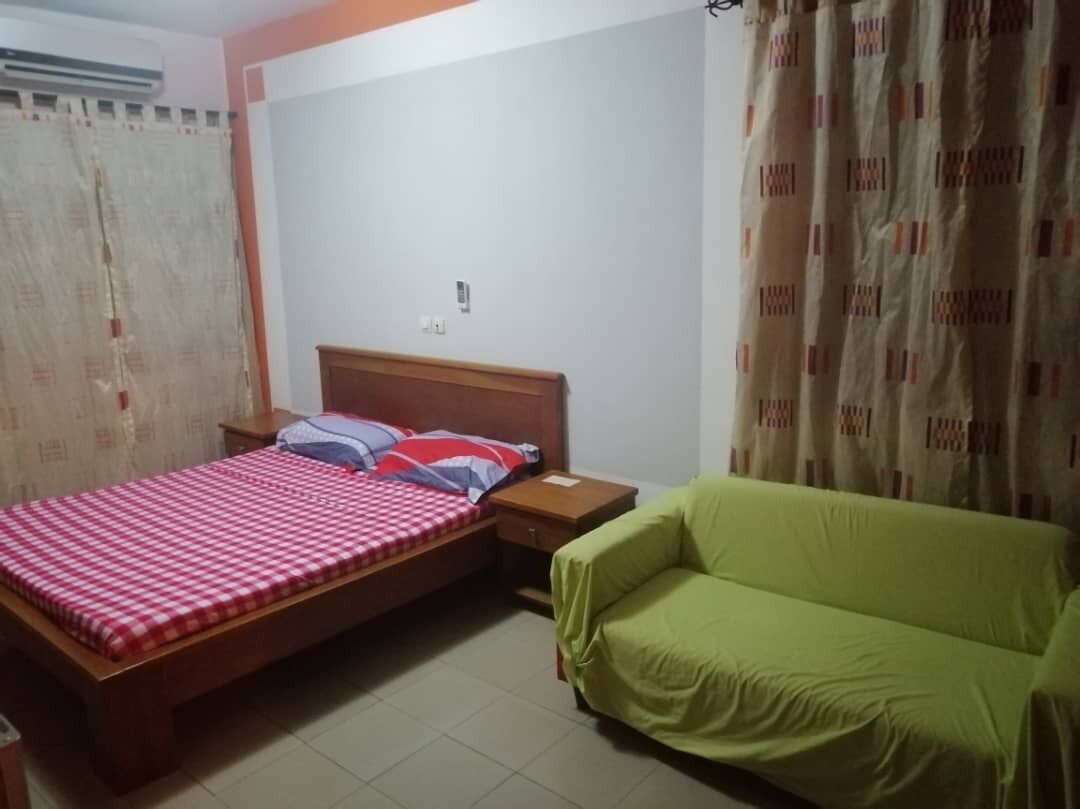 A bedroom with a bed, a green sofa, and a window with curtains.