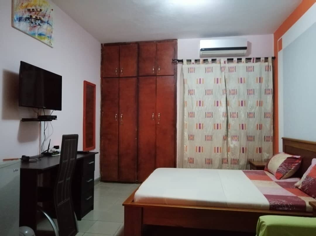 A bedroom with a bed, a desk, a chair, a TV, and a wardrobe.