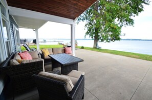 A covered patio with wicker furniture, a view of the water, and a grassy area. - Waters Edge B&B Resort (Geneva)