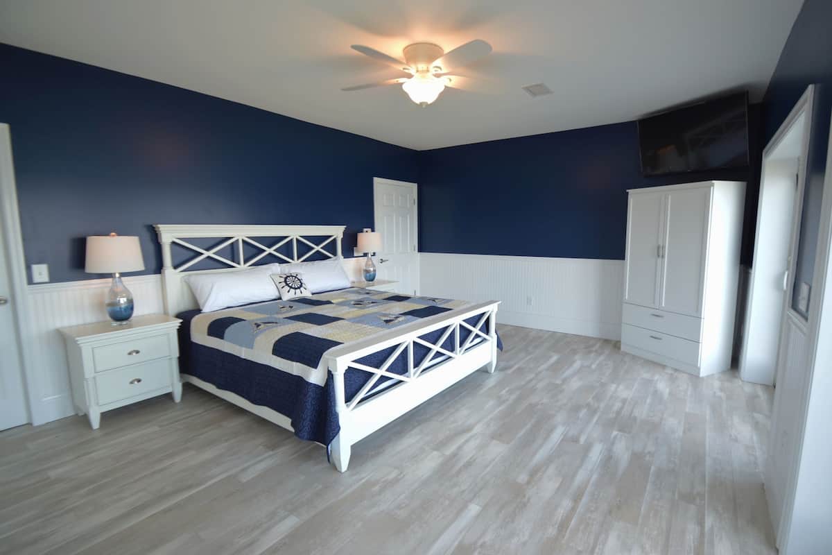 Quarto com cama, mesas de cabeceira, guarda-roupa e ventoinha no teto.
