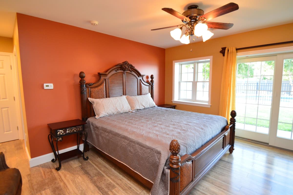 Quarto com cama de madeira, mesa de cabeceira, ventoinha no teto e janela com cortinas.