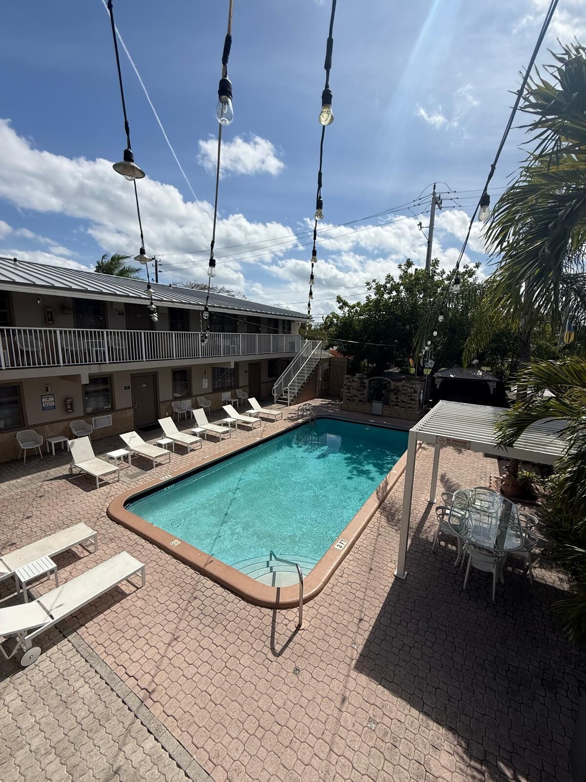 A swimming pool with lounge chairs and a covered seating area, surrounded by a building with a balcony.