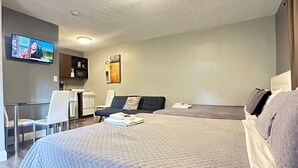 Una habitación de hotel moderna con una cama grande, un televisor montado en la pared, un escritorio y una zona de estar con un sofá.