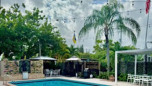 Una piscina con sillas de descanso, rodeada de follaje y un pabellón.